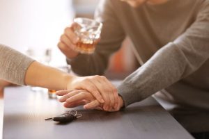 Drunk driving prevention: women taking car keys away from man who has drink in his hand.