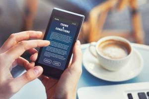 Person holding cell phone to read Terms & Conditions document while having coffee.