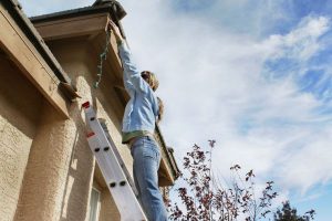 Woman on ladder hanging Christmas lights on outside of house -- one of the leading caused of holiday-related injuries