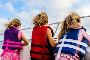 Three girls standing at boat rail in safety vests demonstrate one way to keep children safe when boating.